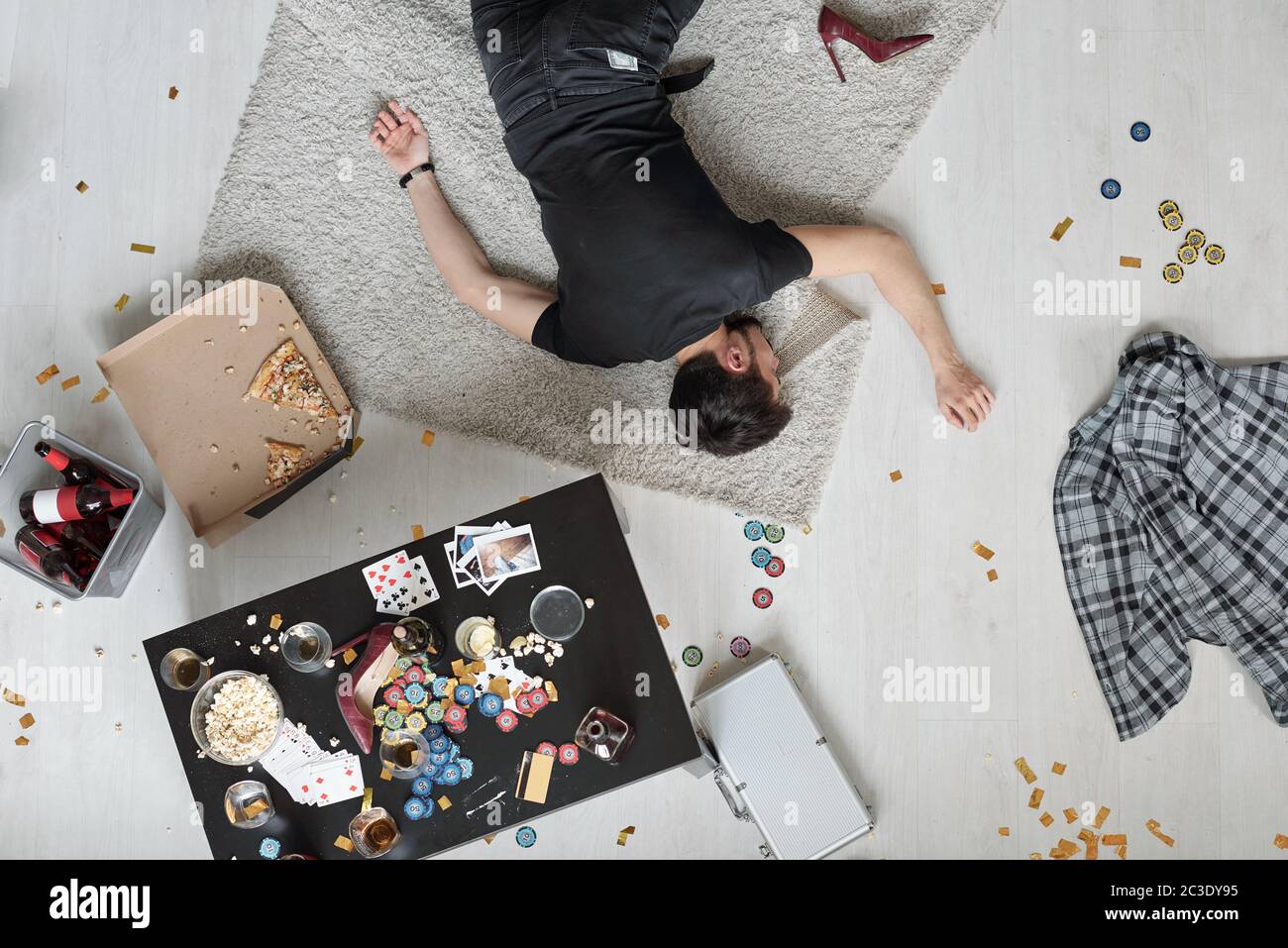 Oben Blick auf den Mann schlafen auf dem Boden unter chaotischen Poker-Chips und Snacks nach der Heimparty Stockfoto