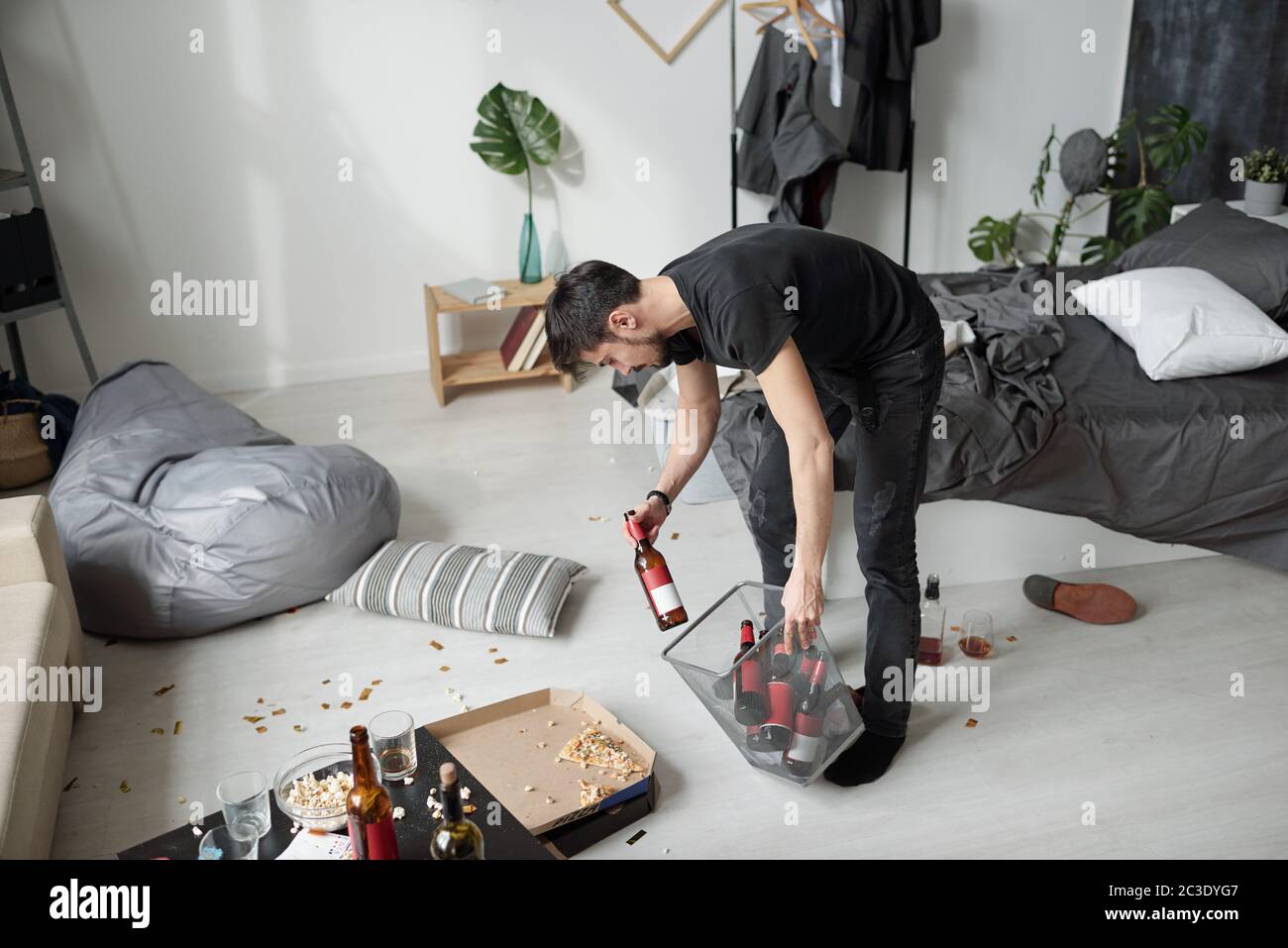Junge Partymaker werfen leere Alkoholflaschen in den Papierkorb, während die Reinigung Zimmer nach der Party Stockfoto