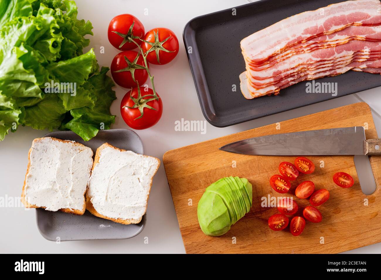 Stillleben Zusammensetzung bestehend aus zwei Sandwiches, frische Tomaten, Salat, Avocado und Tablett mit Speck Scheiben auf Küchentisch Stockfoto