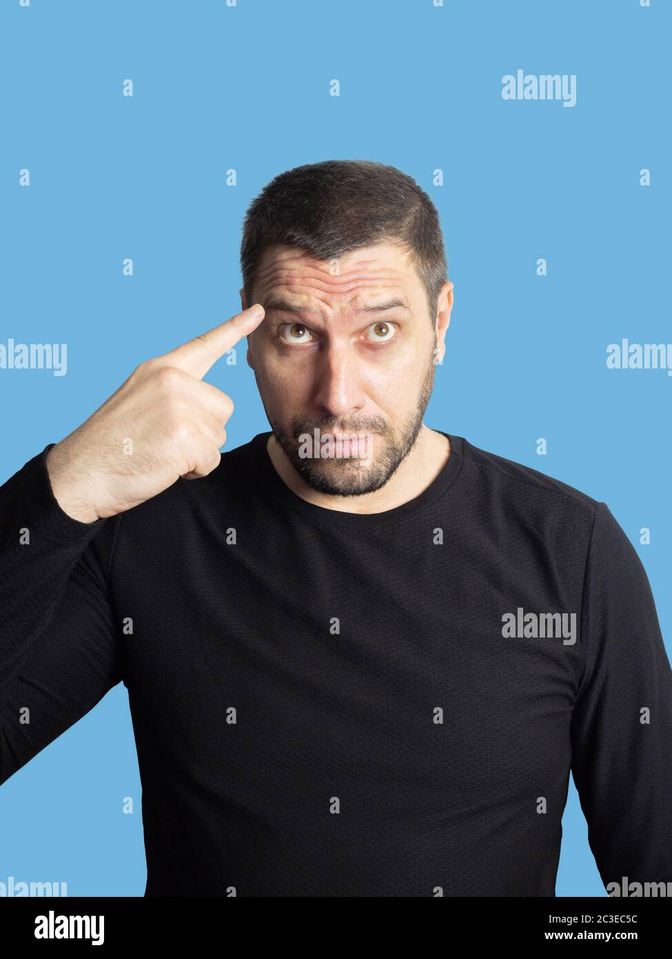 Ein unrasiert Mann mit braunen Augen in einem schwarzen Sweatshirt schaut auf und zeigt einen Finger mit Falten auf seine Stirn Stockfoto