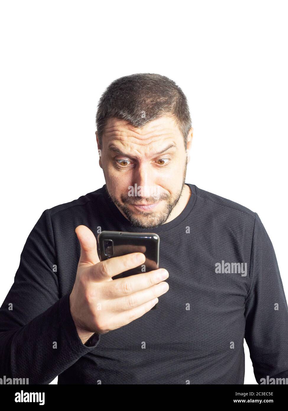 Ein Mann mit Bart und in einem schwarzen Pullover schaut mit erhobener Augenbraue und wulstigen Augen auf das Telefon. Stockfoto