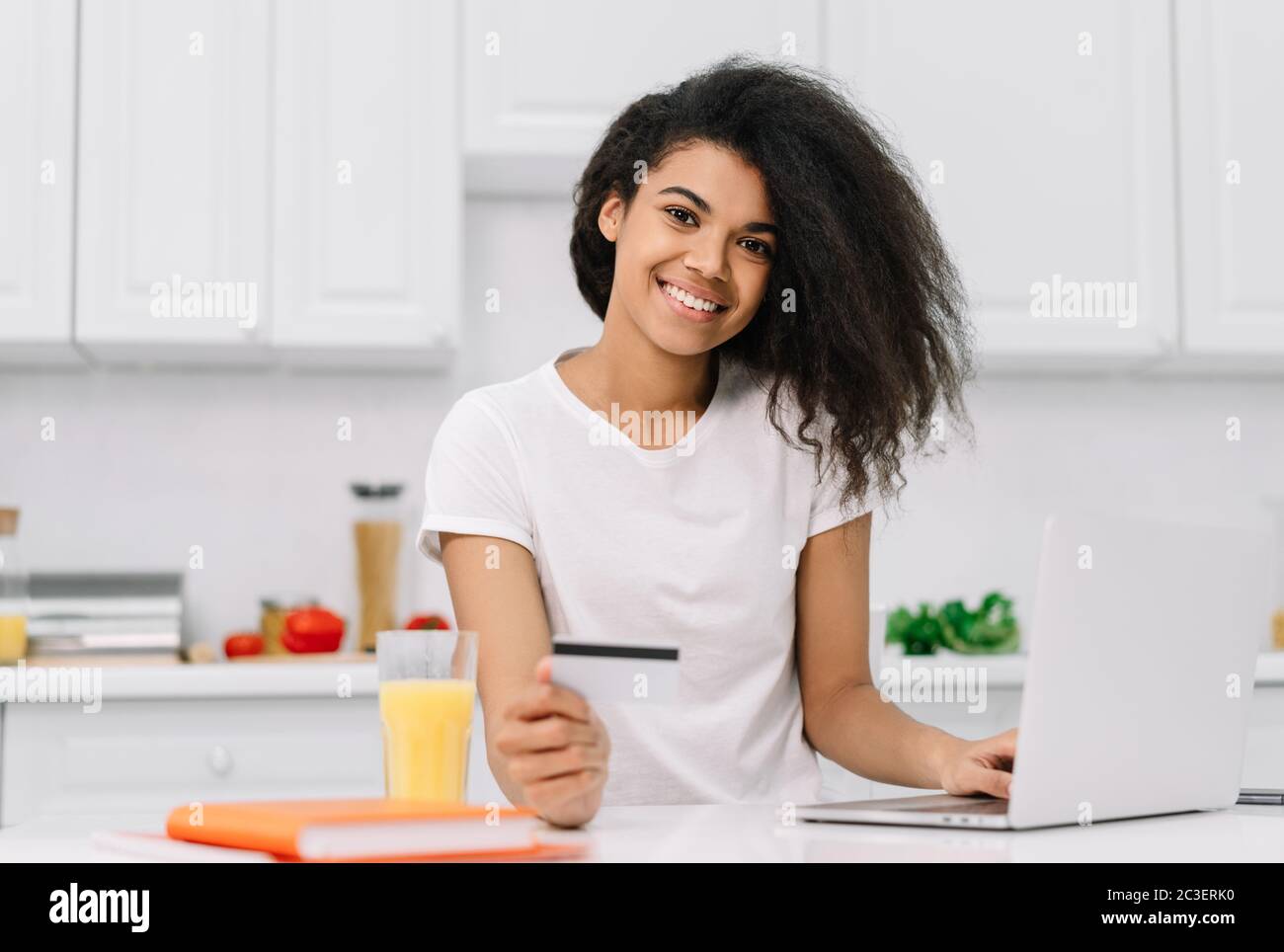 Glückliche afroamerikanische Frau, die online einkauft, Essen bestellt, auf der Küche steht Stockfoto