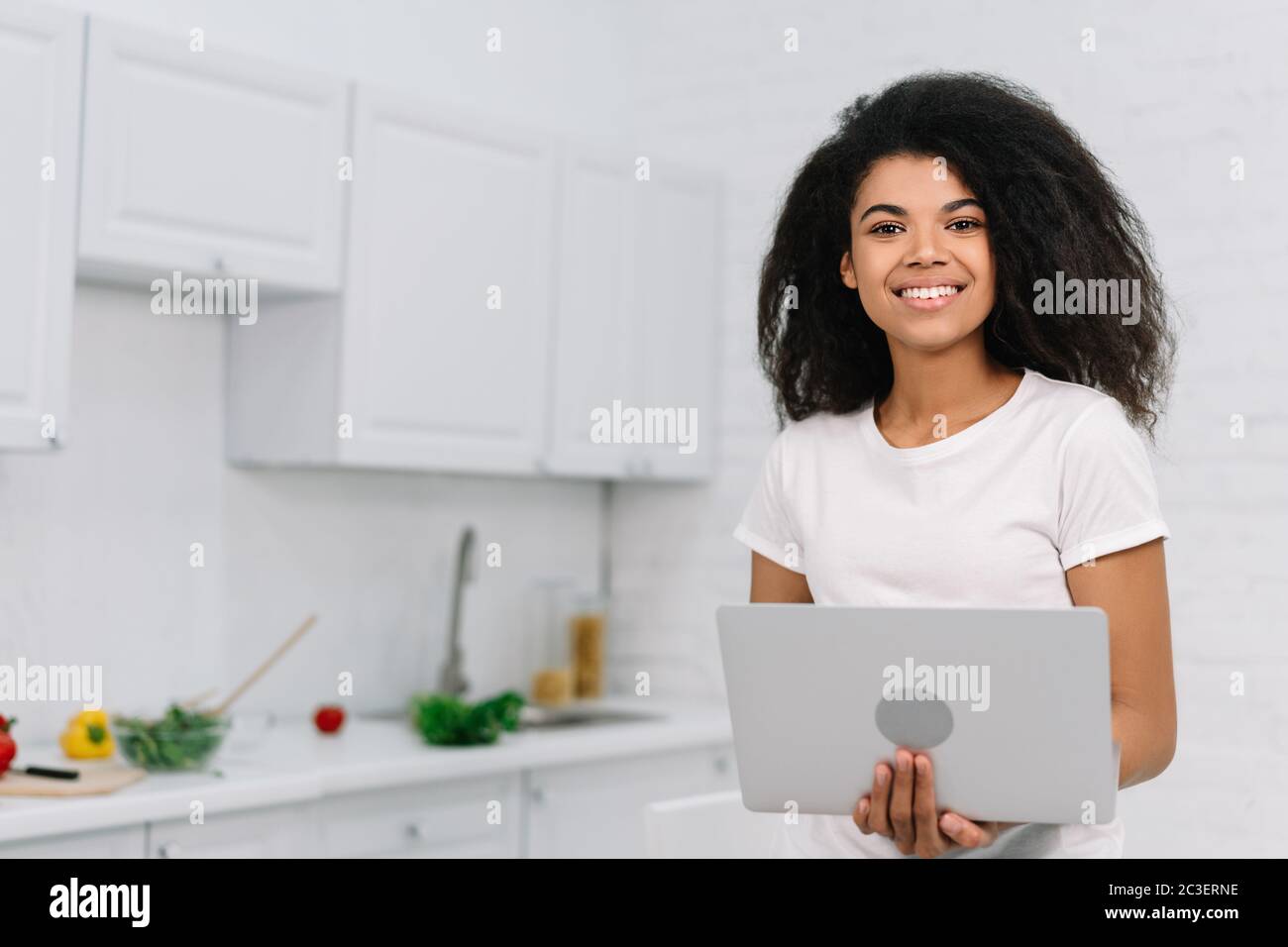 Schöne afroamerikanische Frau mit Laptop-Computer für Online-Shopping mit Bargeld zurück in der Küche stehen. Weibliche Bestellung Lebensmittel online Stockfoto