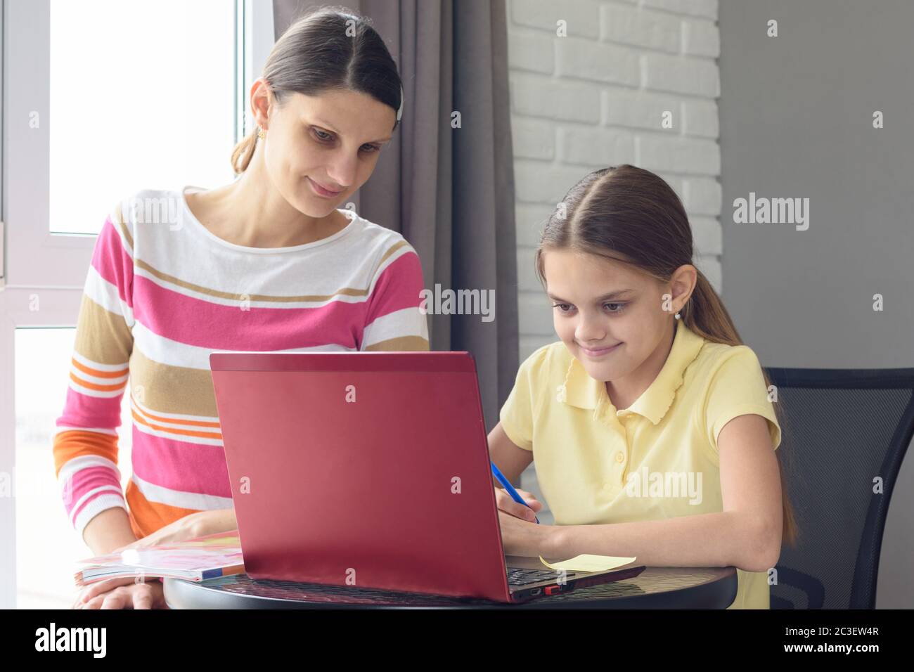 Ein Mädchen und ein Mädchen sitzen an einem Tisch und durchsuchen Webseiten in einem Laptop Stockfoto