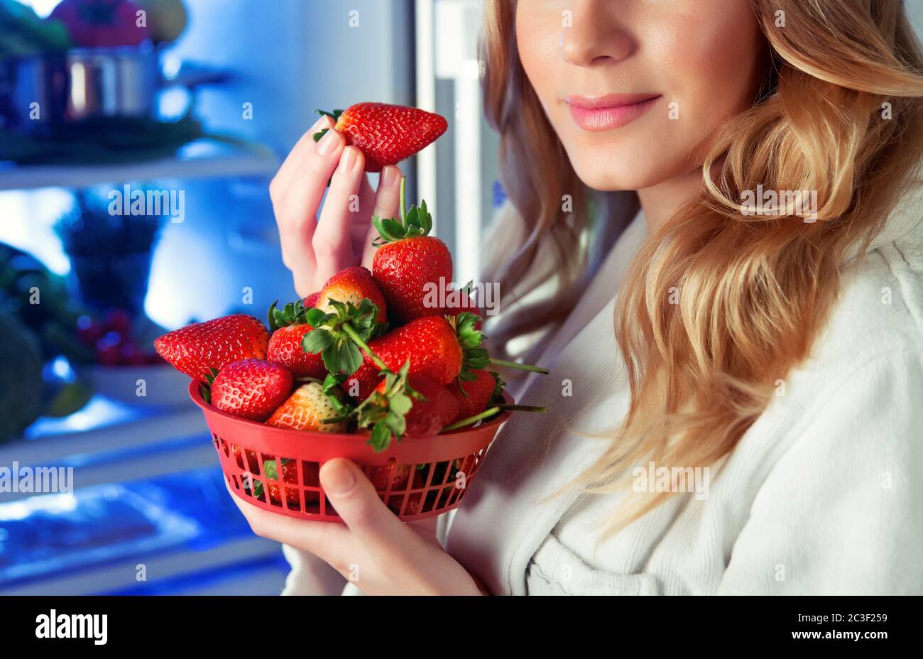 Porträt einer schönen blonden Frau mit Freude essen frische leckere Erdbeeren in der Nähe des offenen Kühlschrank, gute Auswahl, vegetarische Gerichte, Gewichtsverlust Stockfoto