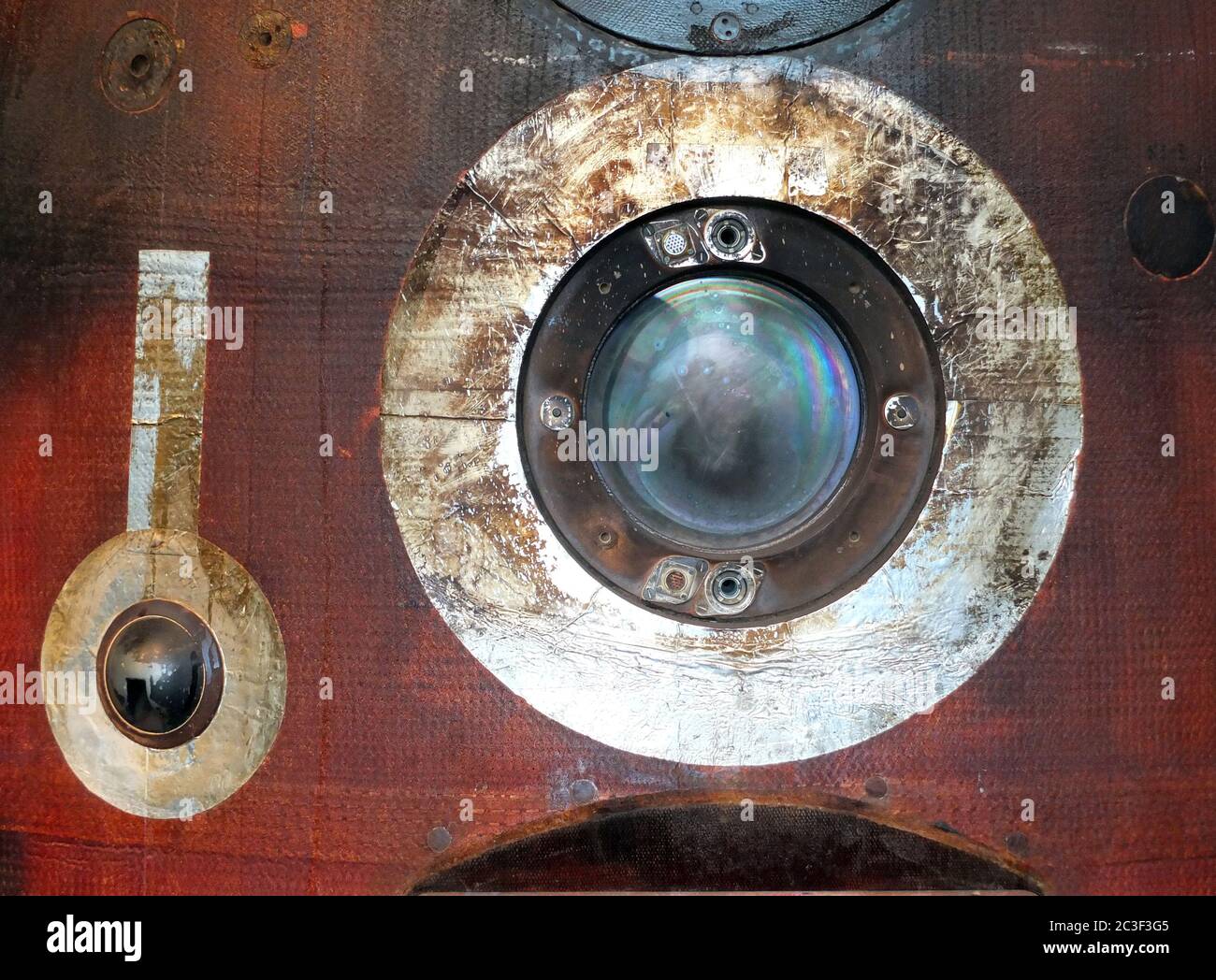 Nahaufnahme eines runden Portholes auf einem gebrauchten russischen Raumfahrt-Wiedereinstieg mit gebranntem rotem und schwarzem Stahlblech Stockfoto