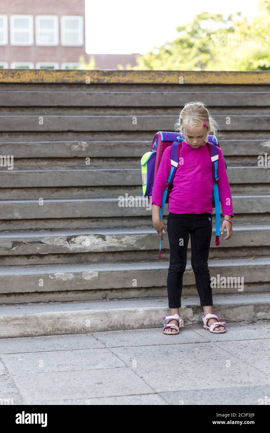 Mädchen (7) mit Tasche traurig vor ihrer Schule, Kiel, Deutschland Stockfoto