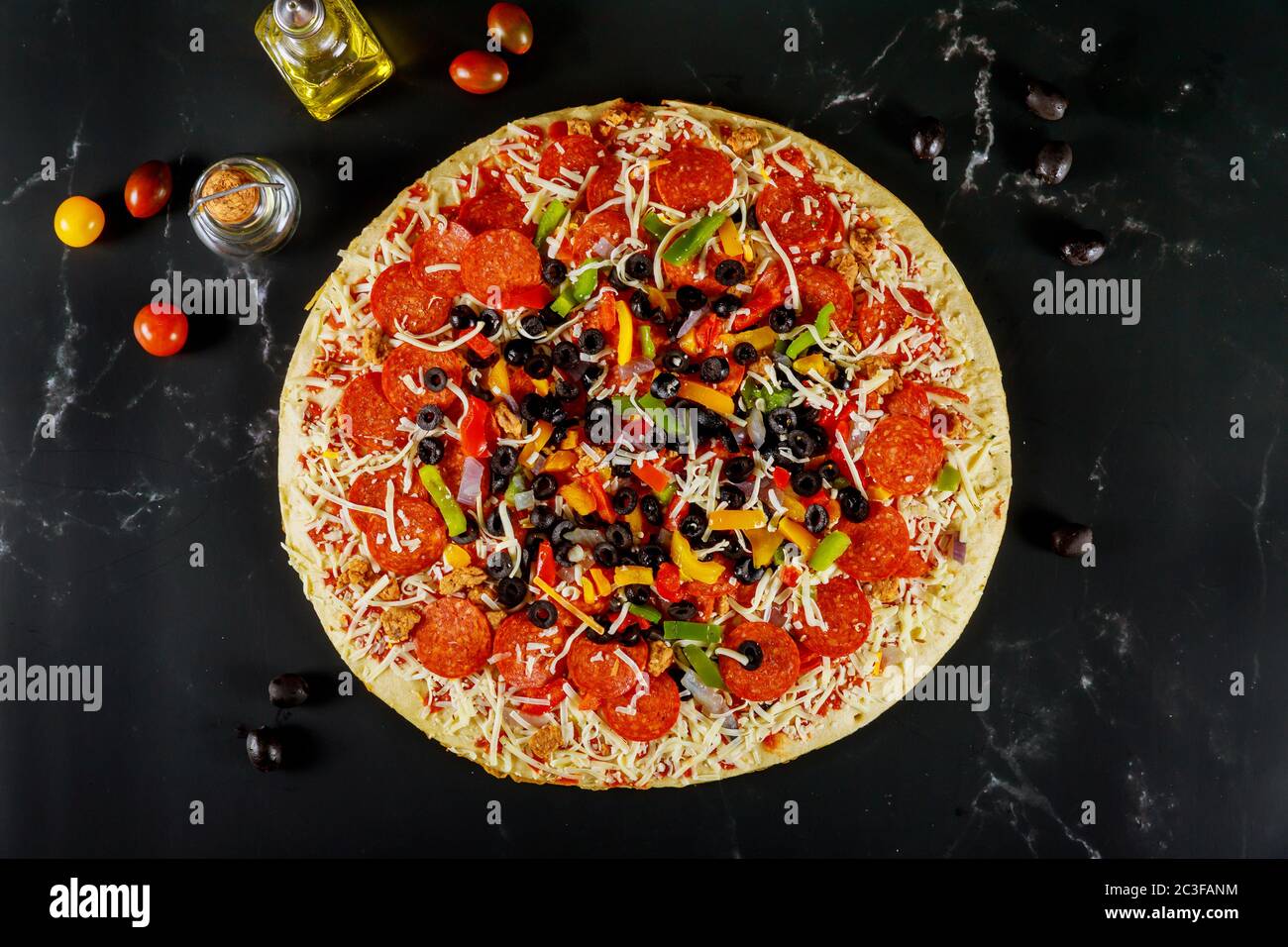 Extra große Pizza mit Oliven, Pfefferoni und Tomaten auf schwarzem Hintergrund. Stockfoto