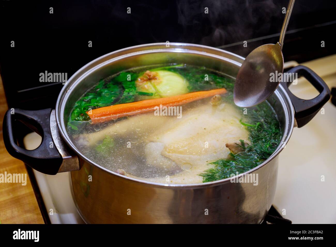 Zubereitung von Hühnerbrühe mit Gemüse in einem Stahltopan mit Löffel. Stockfoto