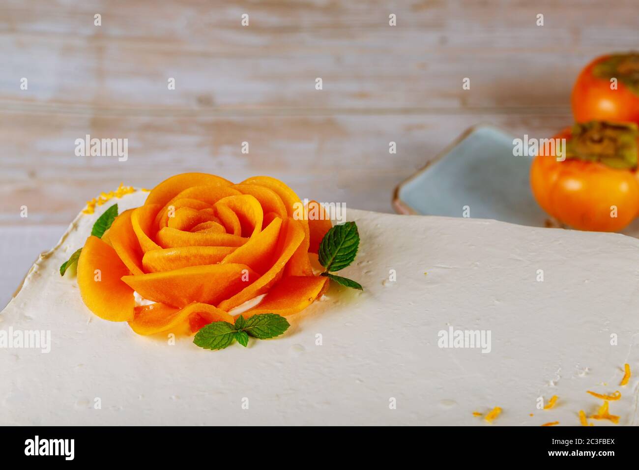 Karottenkuchen mit Frischkäse Zuckerguss bedeckt und mit einer Rose aus Persimmon geschnitten dekoriert. Stockfoto