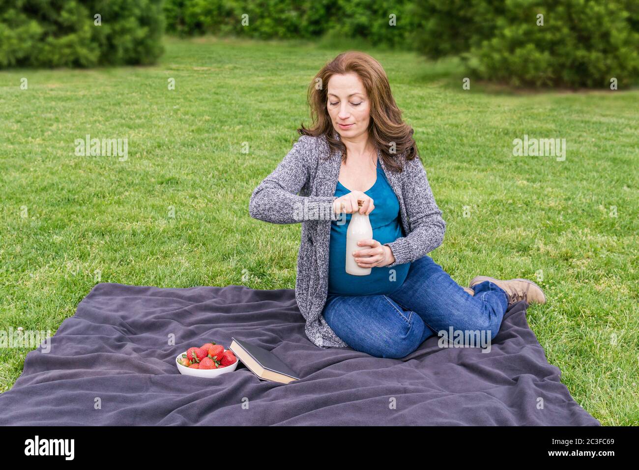 Schwangere Frau mit einer Flasche Milch auf einem grünen Feld in einem Park. Stockfoto