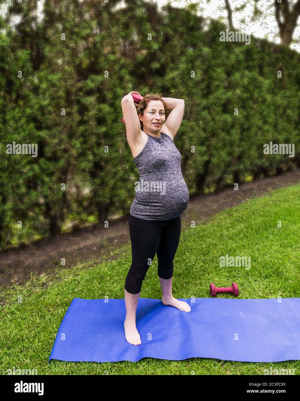 Gesunde schwangere Frau, die Yoga mit Hanteln in der Natur im Freien macht. Stockfoto