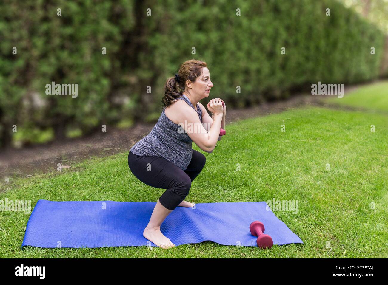 Gesunde schwangere Frau, die Yoga mit Hanteln in der Natur im Freien macht. Stockfoto