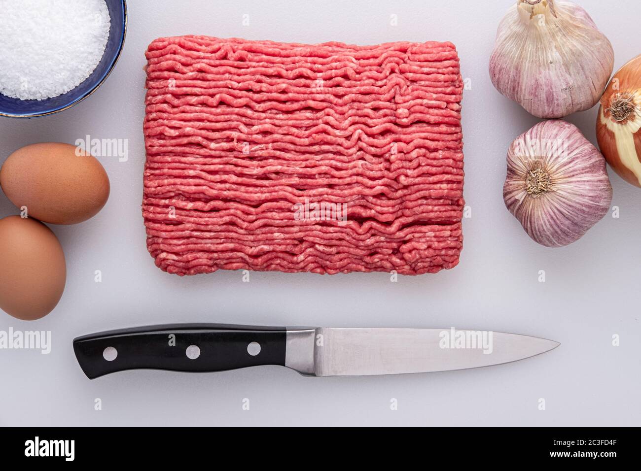 Platte aus rohem mageren Hackfleisch, aus der Fleischtheke, mit koscheres Salz, Knoblauch, Zwiebeln auf einem Schneidebrett mit einem Küchenmesser Stockfoto