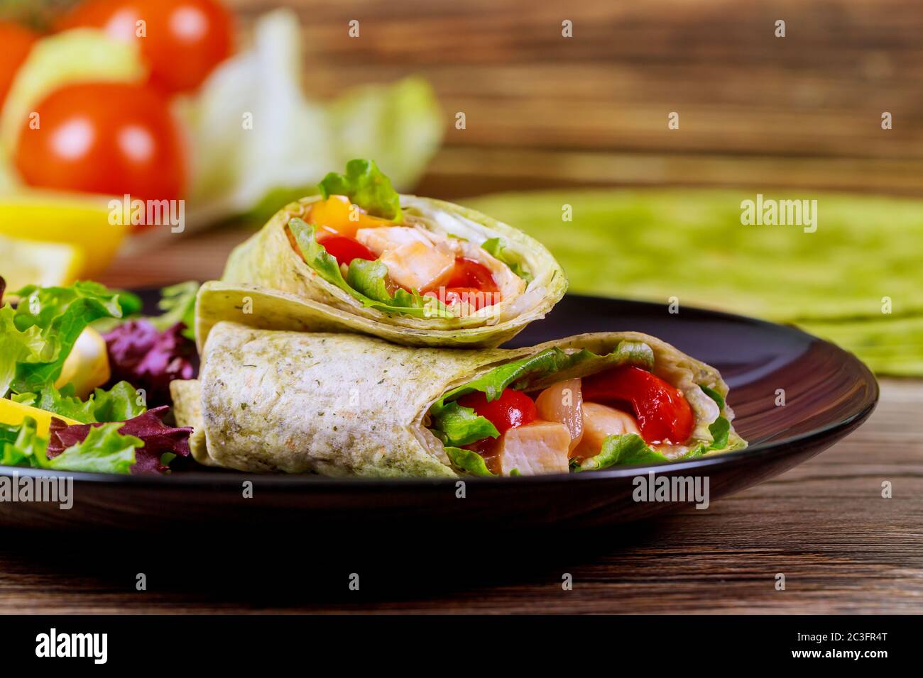 Spinat Wrap mit Fleisch und Gemüse auf schwarzem Teller mit grünen Tortillas. Stockfoto
