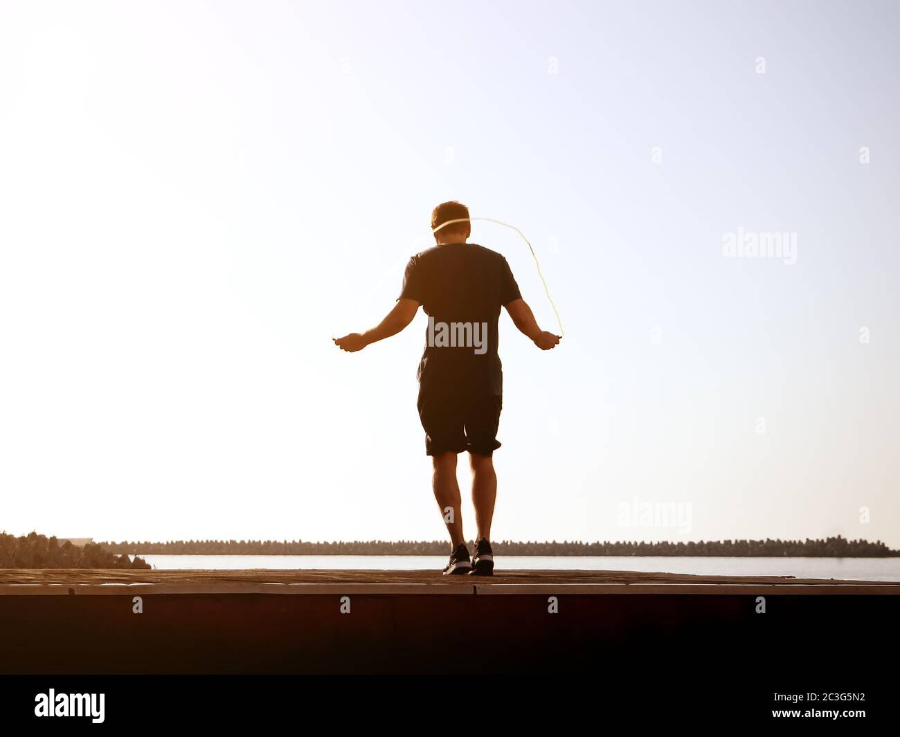 Mann in Shorts springt an einem sonnigen Tag am hintergrundigen Himmel auf einem Seil. Künstlerische Wirkung. Verschwommenes Bild Stockfoto