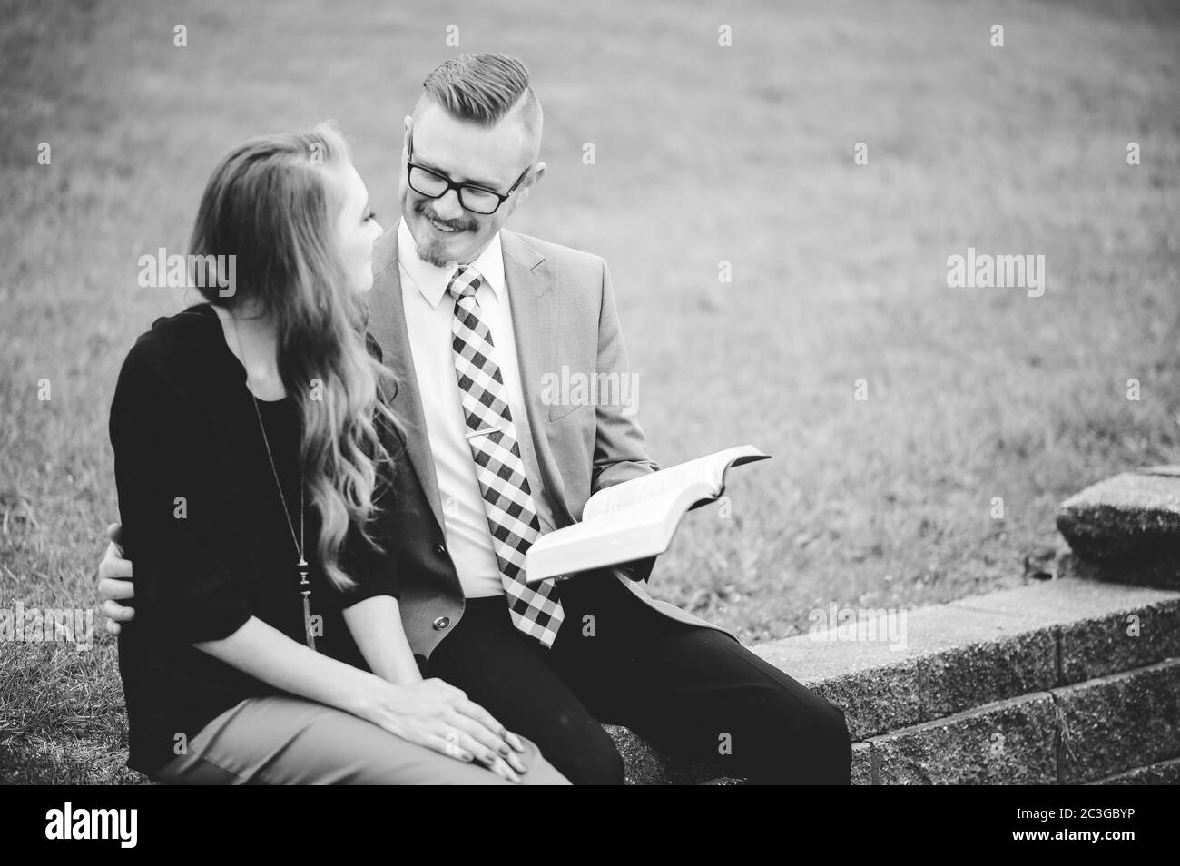 Graustufen eines Paares auf Blöcken sitzend und liebevoll lesend Ein Buch Stockfoto