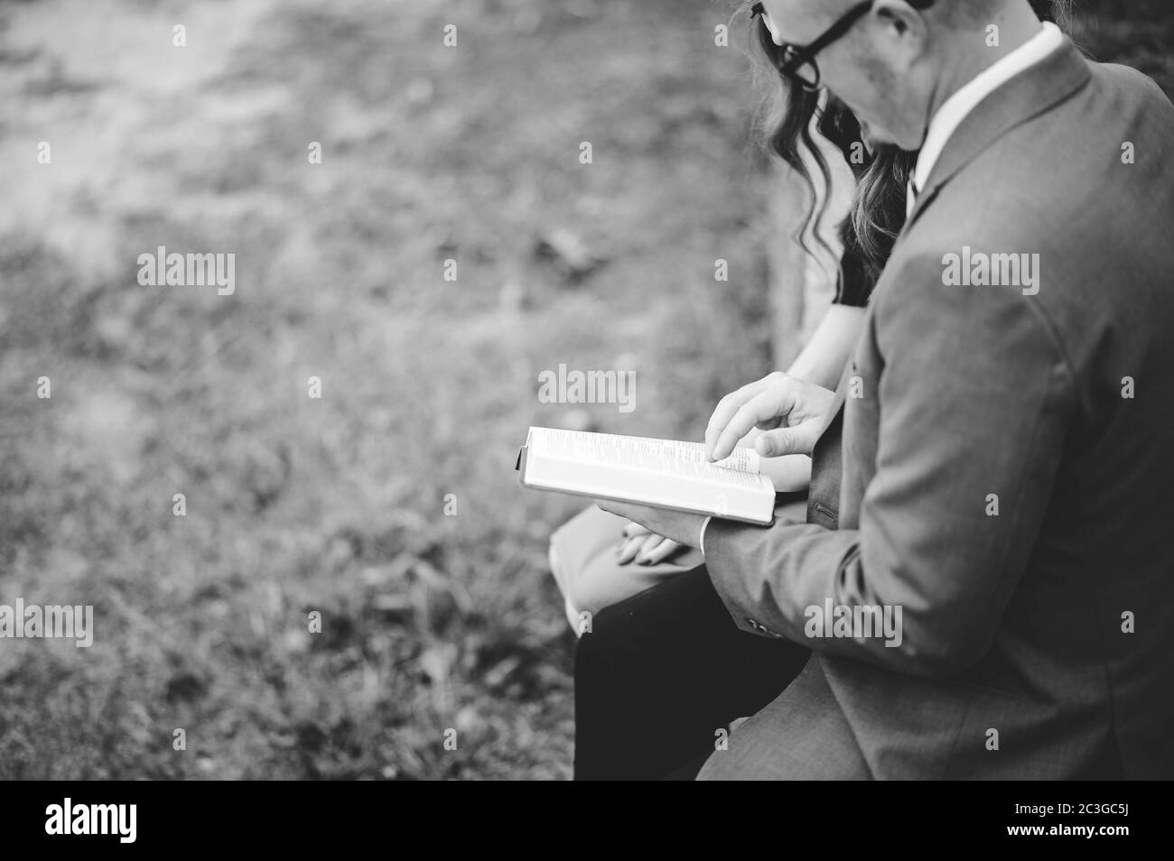 Draufsicht Graustufen eines Paares, das in einem Garten sitzt Und liebevoll zusammen ein Buch lesen Stockfoto
