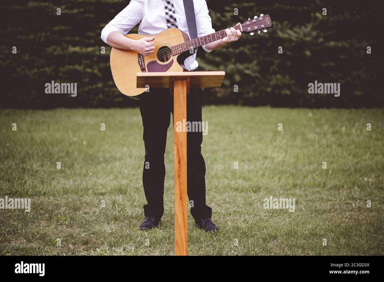 Junger Mann in einem Park, der eine Gitarre hält und spielt Ein Lied aus dem christlichen Gesangbuch Stockfoto