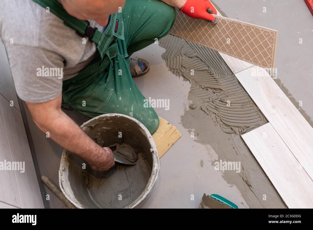 Ein Bauarbeiter schmiert den Boden der Keramikfliesen mit einer Metallkelle mit Spezialleim. Stockfoto