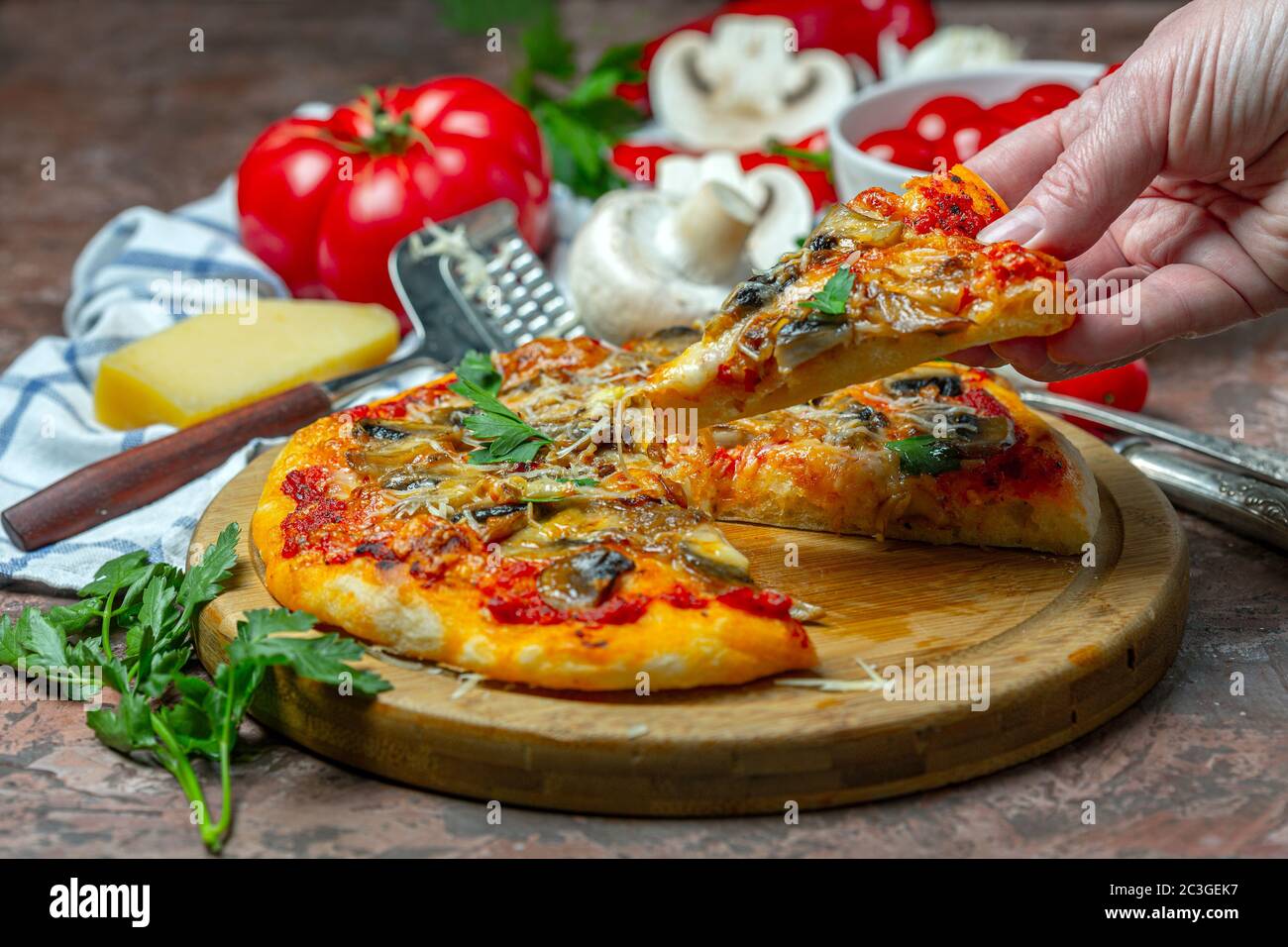 Hand mit einer Scheibe Pizza mit Pilzen und Tomaten. Stockfoto