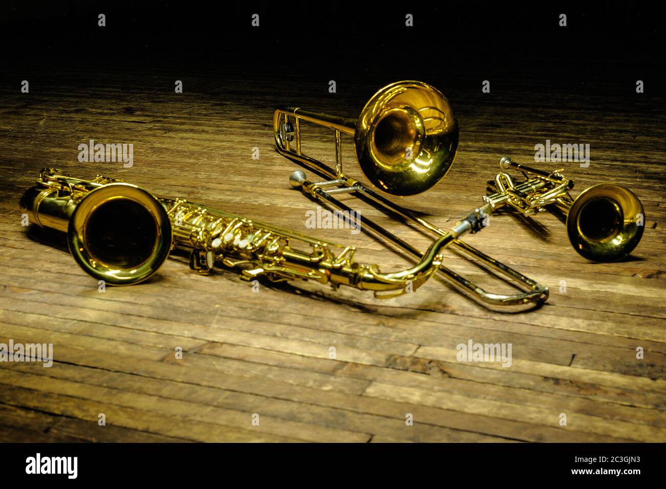 Gelbe Blas- und Blasinstrumente - Saxofon, Posaune, Trompete auf Holzbühne mit Hintergrundbeleuchtung Stockfoto