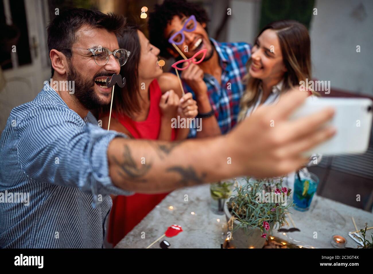 Junge Paare mit lustigen Masken, die Selfie im Garten des Cafés machen Stockfoto