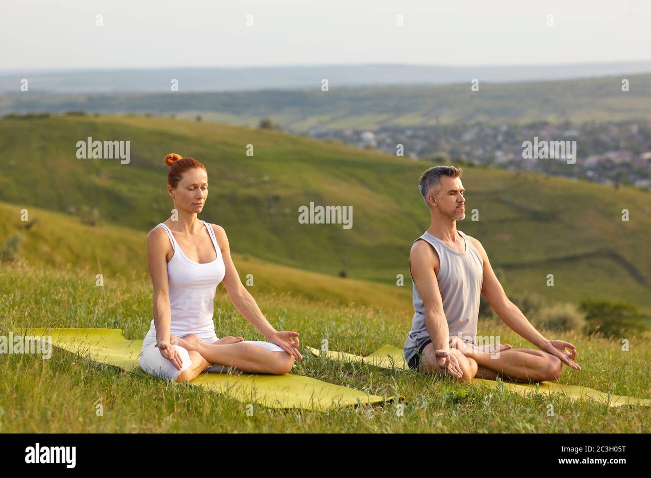 Yoga-Meditation üben. Ein paarvermähltes Paar praktiziert Yoga-Meditation in Lotushaltung, die im Sommer im Frühjahr auf dem Gras auf der Natur sitzt. Stockfoto