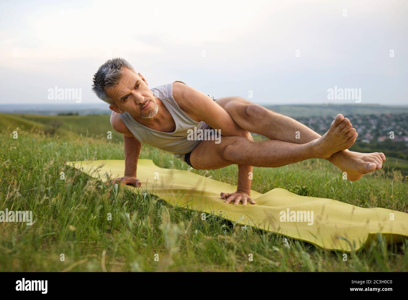 Im Sommer Yoga auf dem Rasen. Reife grauhaarige Mann praktiziert Yoga Balance Pose in der Natur Stockfoto