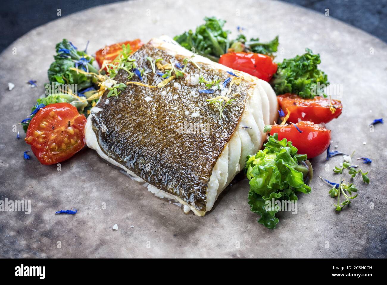 Gourmet-gebratenes europäisches Skrei-Kabeljau-Fischfilet mit Kalette und Tomaten als Nahaufnahme auf einem modernen Design-Teller Stockfoto
