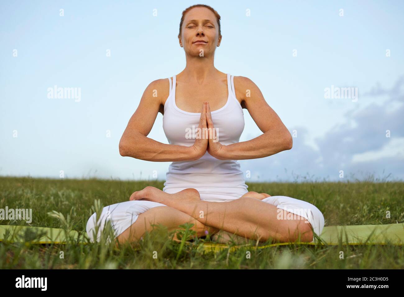 Yoga Frau Meditation in der Natur. Athletische Frau in weißer Kleidung meditiert in Lotusposition auf dem Gras im Sommer Frühling. Stockfoto