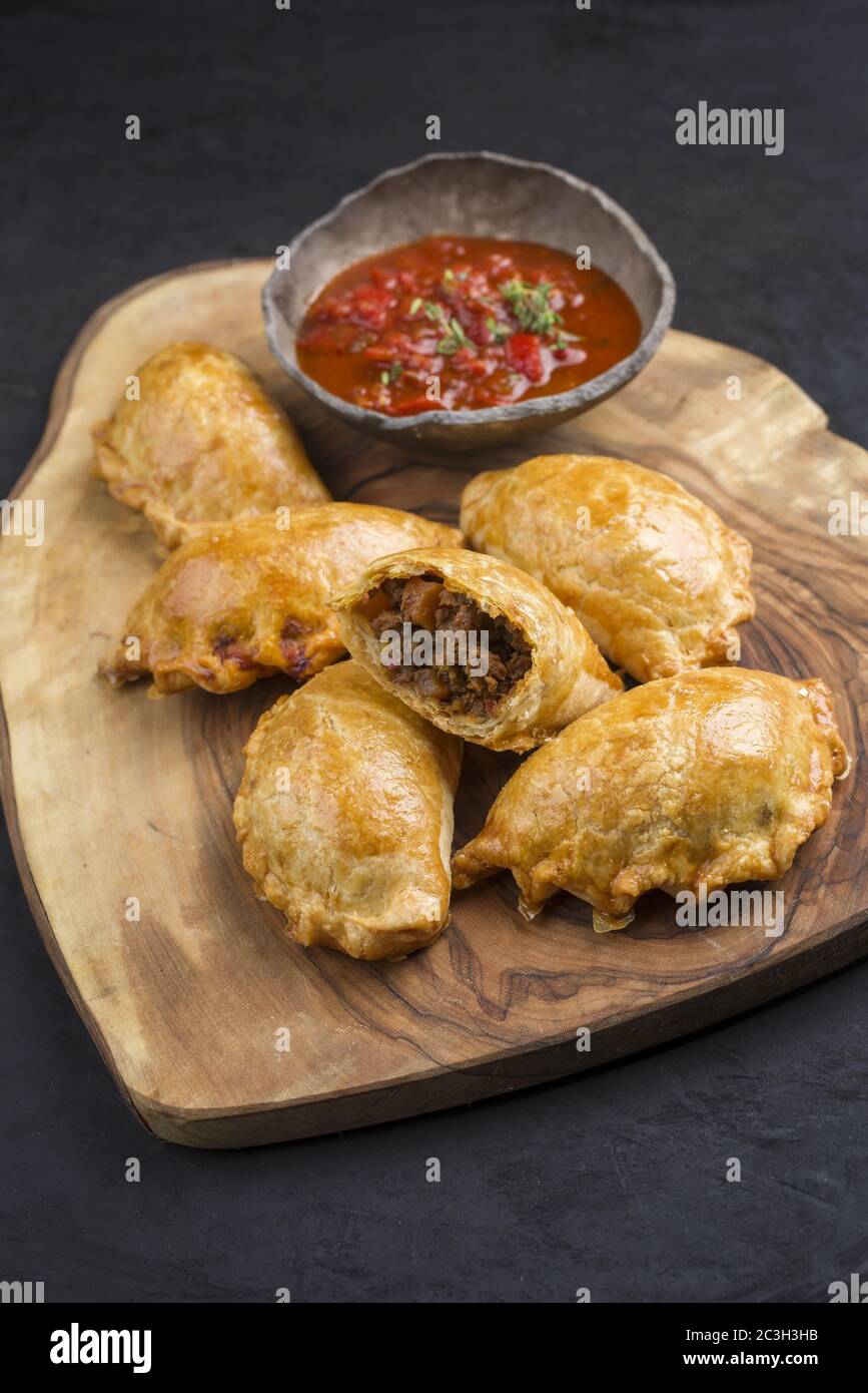 Traditionelle südamerikanische Empanada de Carne mit einem Chili-Dip als Nahaufnahme auf einem rustikalen Holzbrett angeboten Stockfoto
