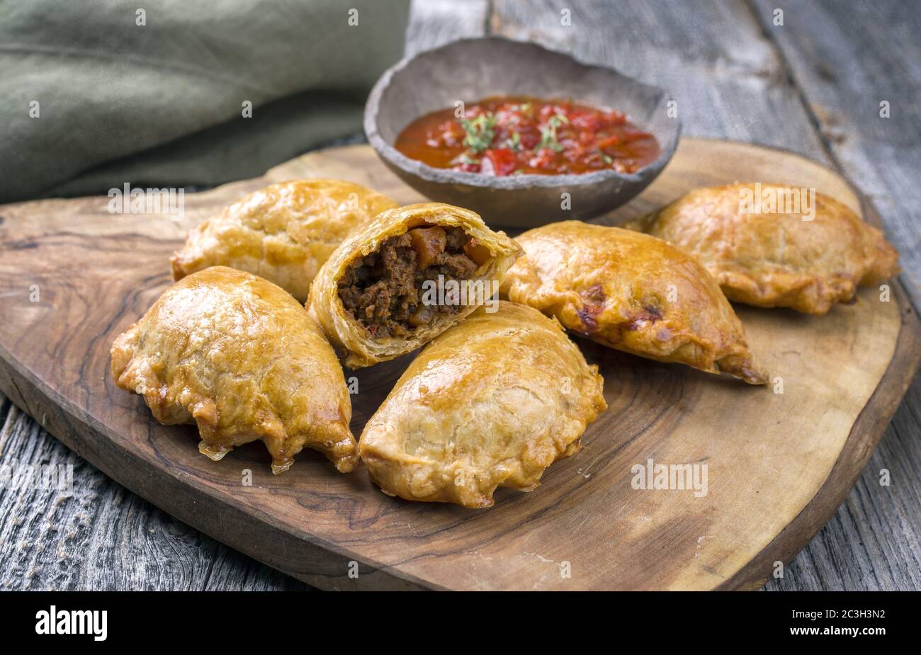 Traditionelle südamerikanische Empanada de Carne mit einem Chili-Dip als Nahaufnahme auf einem rustikalen Holzbrett angeboten Stockfoto
