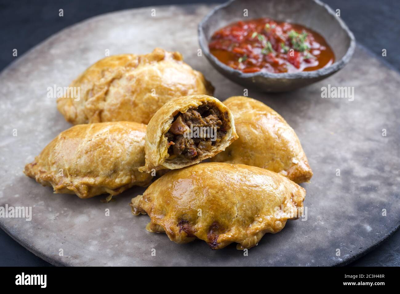 Traditionelle südamerikanische Empanada de Carne mit einem Chili-Dip als Nahaufnahme auf einem rustikalen, modernen Design-Teller angeboten Stockfoto