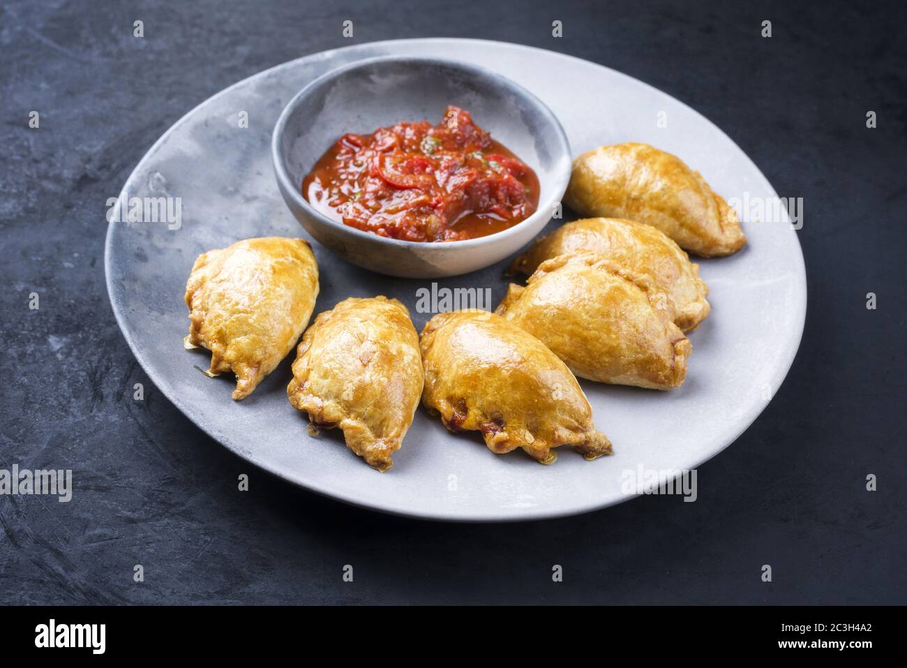 Traditionelle südamerikanische Empanada de Carne mit einem Chili-Dip als Nahaufnahme auf einem modernen Design-Teller angeboten Stockfoto