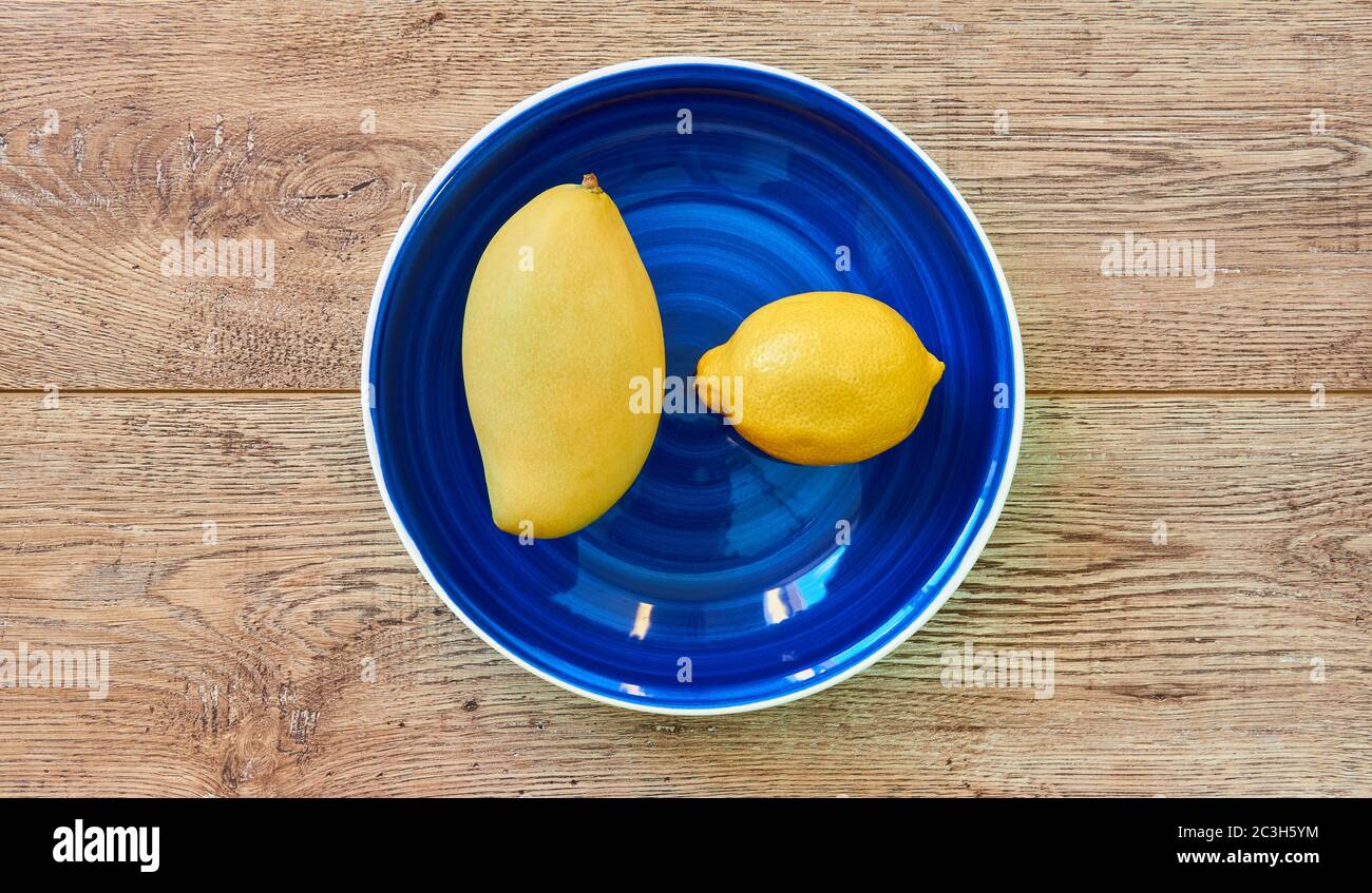 Gelbe Früchte - Zitrone und Mango - auf einem blauen Teller auf einer Holzplatte Stockfoto