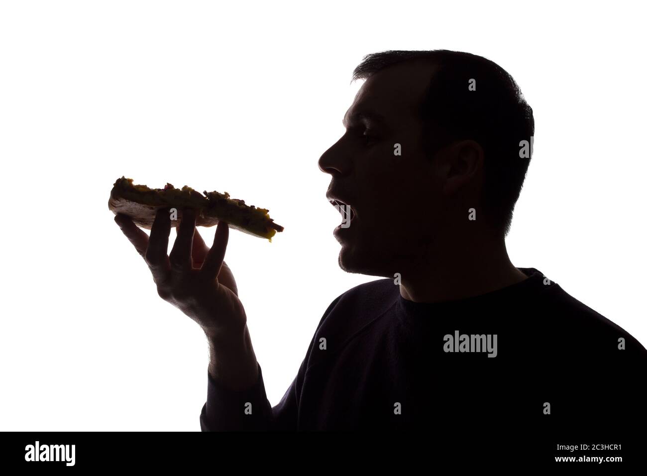 Porträt eines jungen Mannes essen eine Pizza in der Hand, unrasiert, Seitenansicht - dunkel isoliert Silhouette Stockfoto
