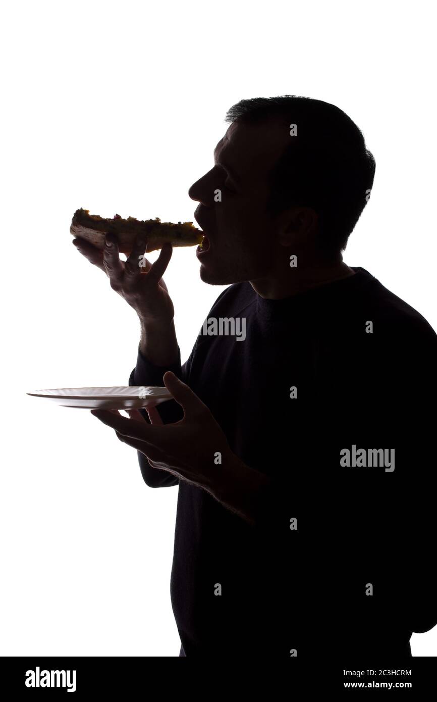 Porträt eines jungen Mannes essen eine Pizza in der Hand, unrasiert, Seitenansicht - dunkel isoliert Silhouette Stockfoto