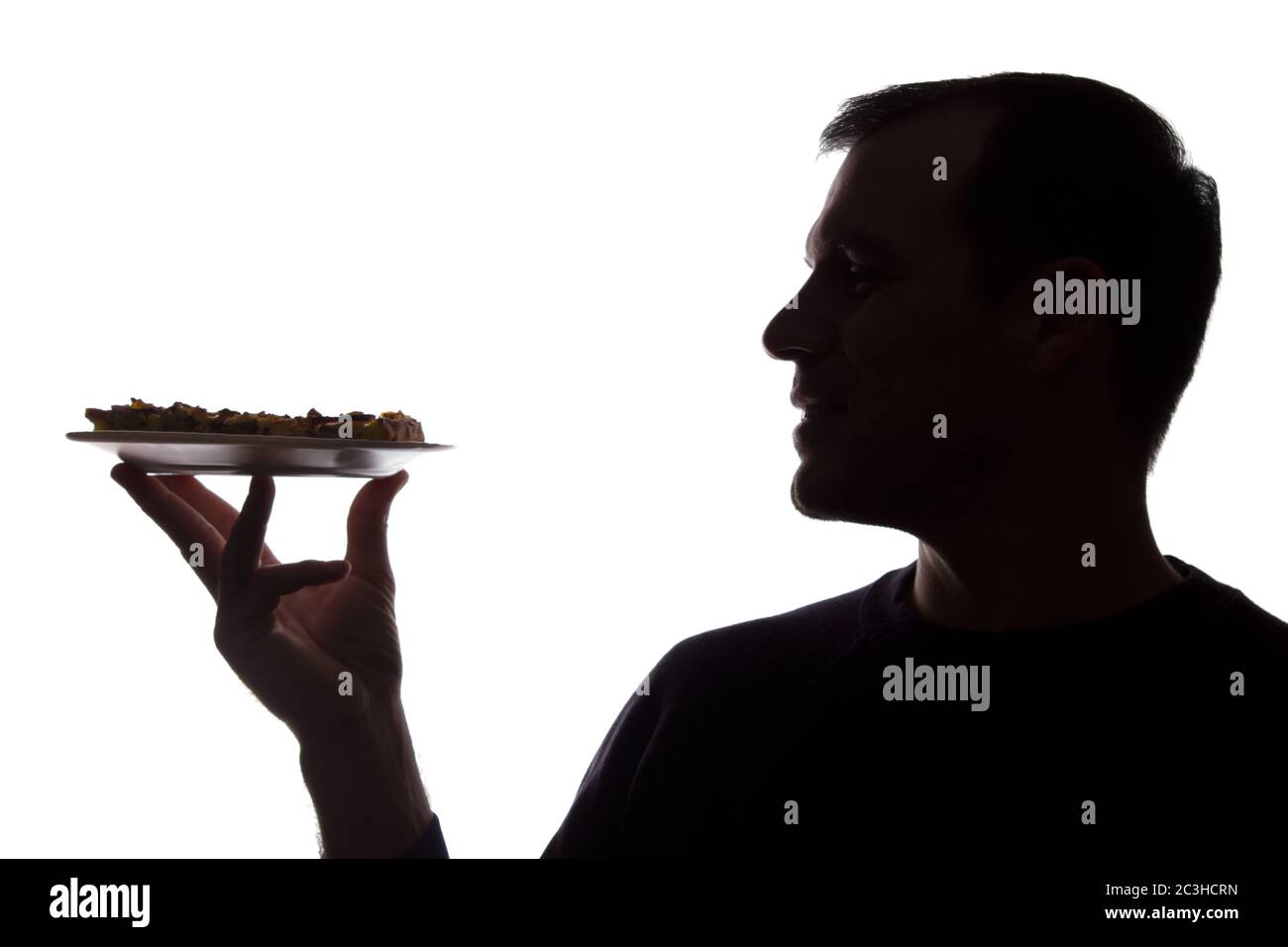 Portrait Lächeln junger Mann mit Pizza auf einem Teller in der Hand, unrasiert, Seitenansicht - dunkel isoliert Silhouette Stockfoto