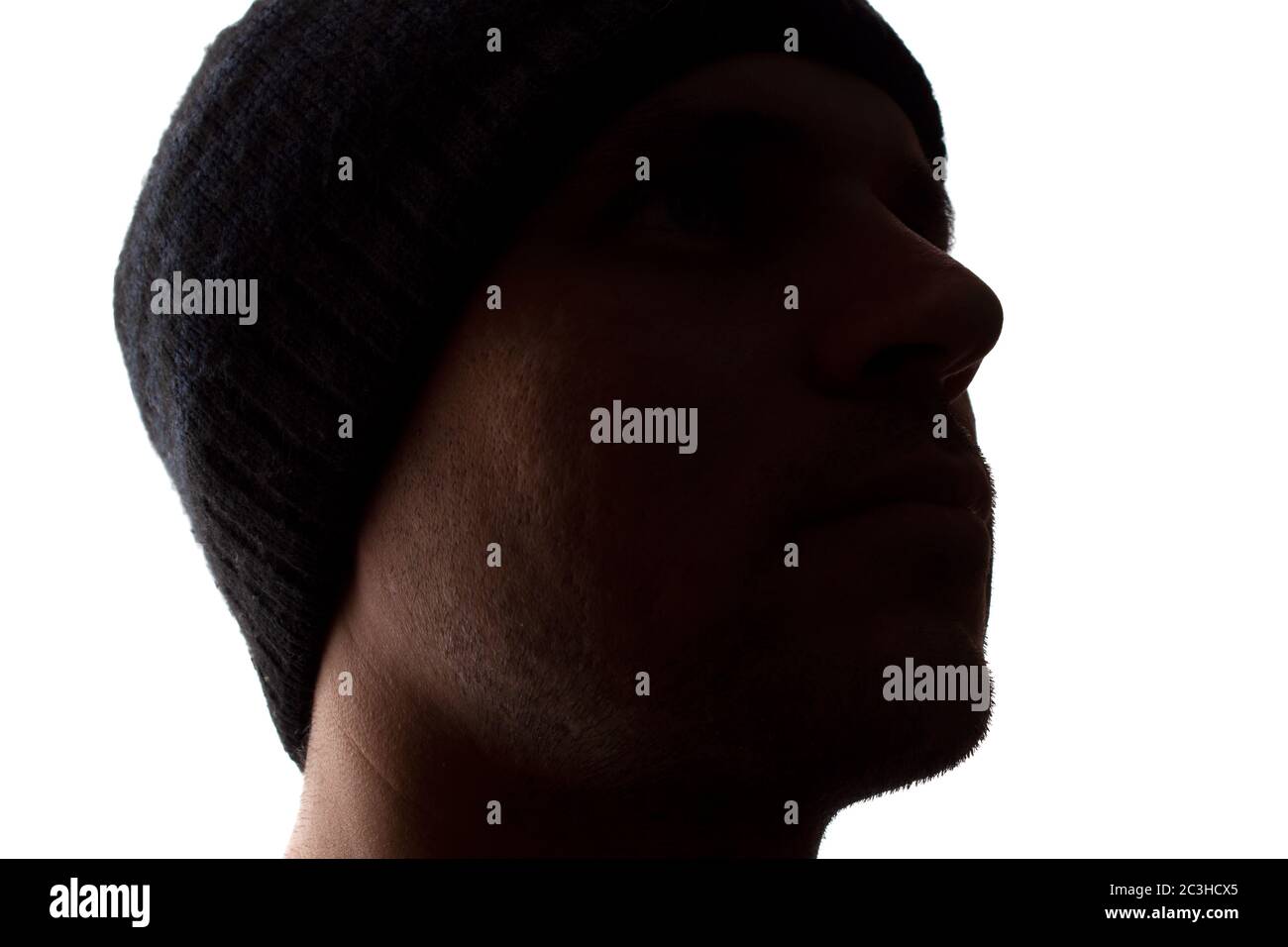 Porträt eines jungen Mannes, unrasiert, Seitenansicht in Mütze - dunkel isolierte Silhouette Stockfoto
