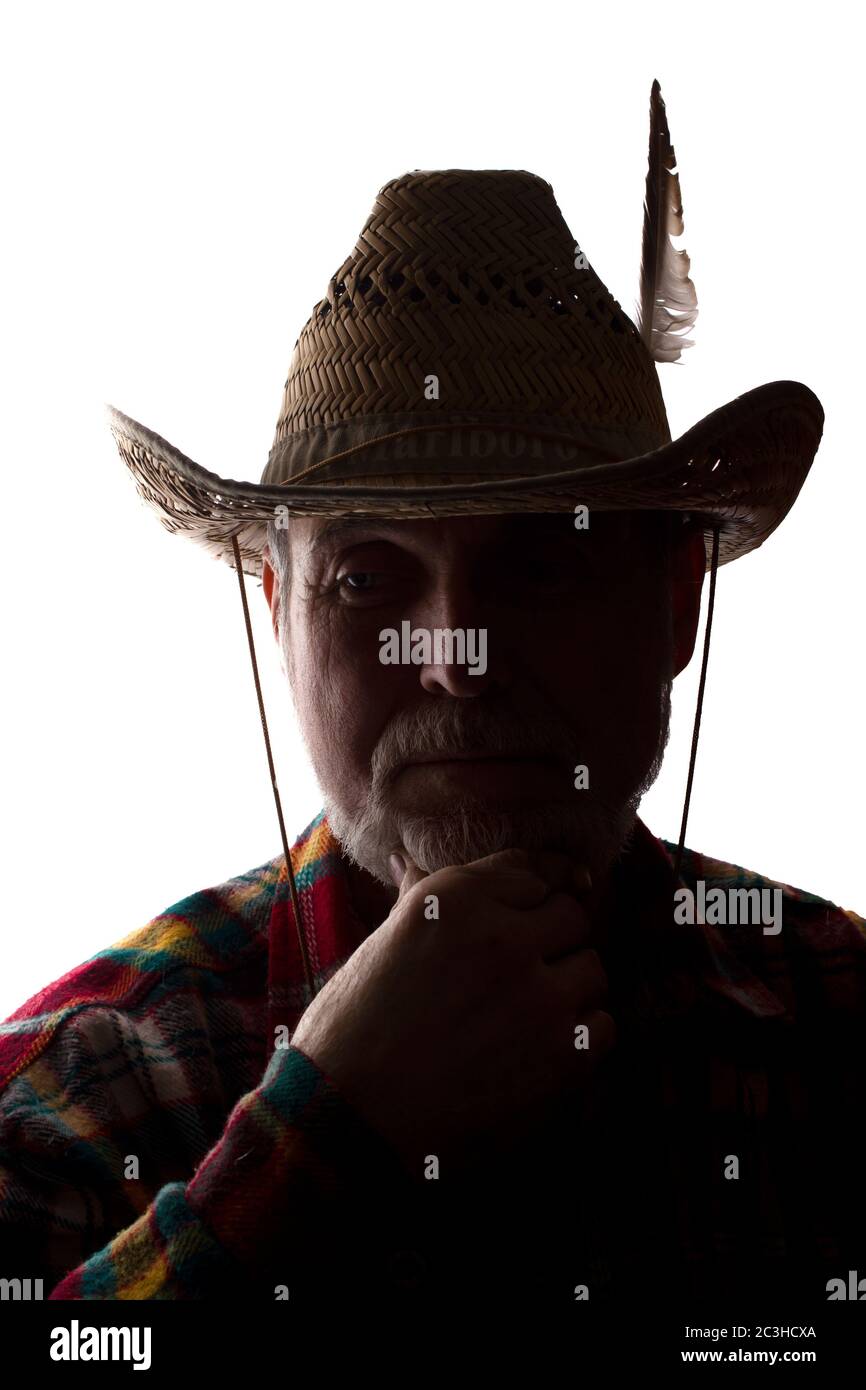 Porträt eines nachdenklichen alten Mannes in einem Cowboy-Hut mit einer Feder, mit einem Bart, Vorderansicht - dunkel isoliert Silhouette Stockfoto
