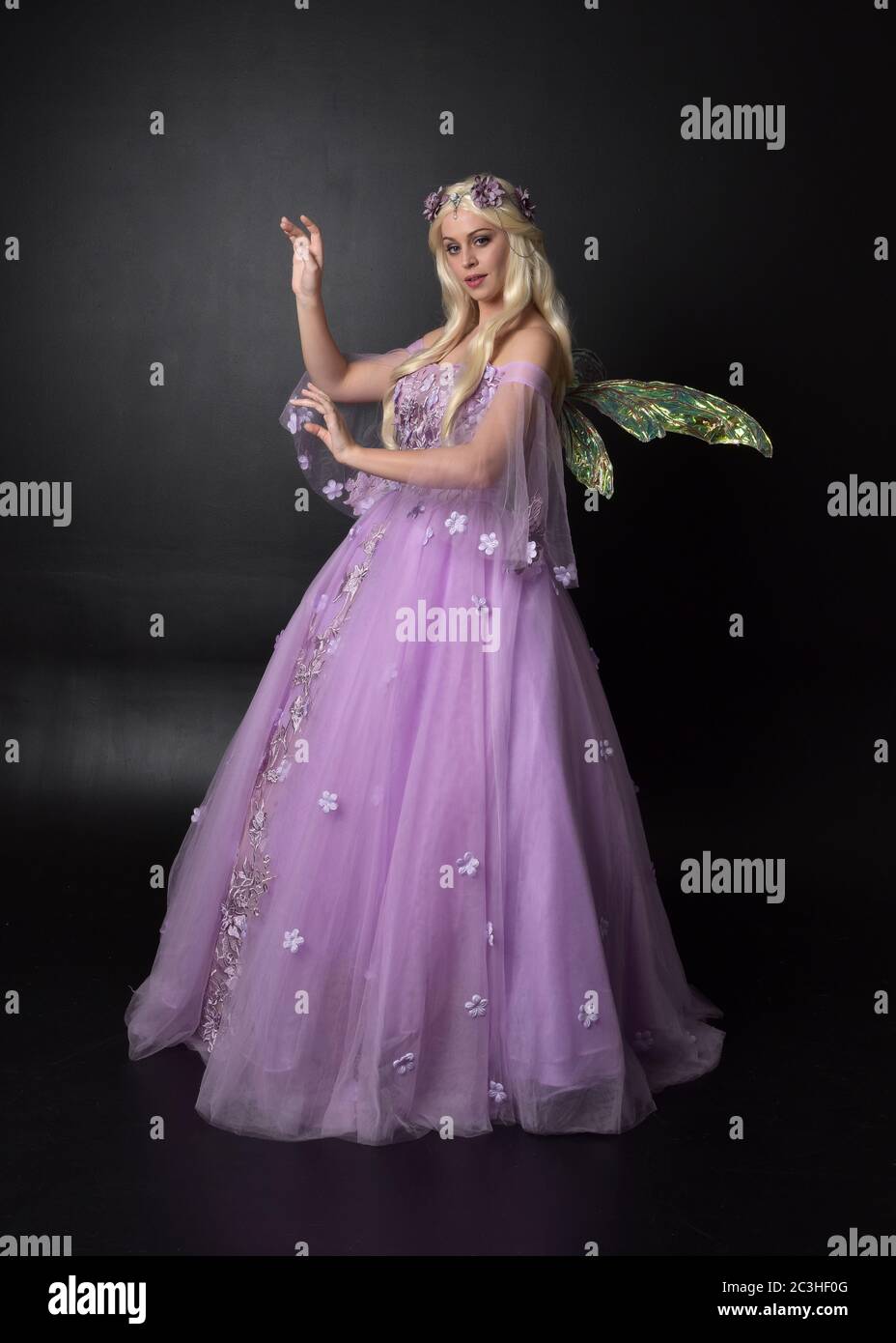 Portrait einer schönen blonden Fee trägt lila Fantasy-Kleid mit Flügeln. In voller Länge stehende Pose, isoliert vor einem Studio-Hintergrund. Stockfoto