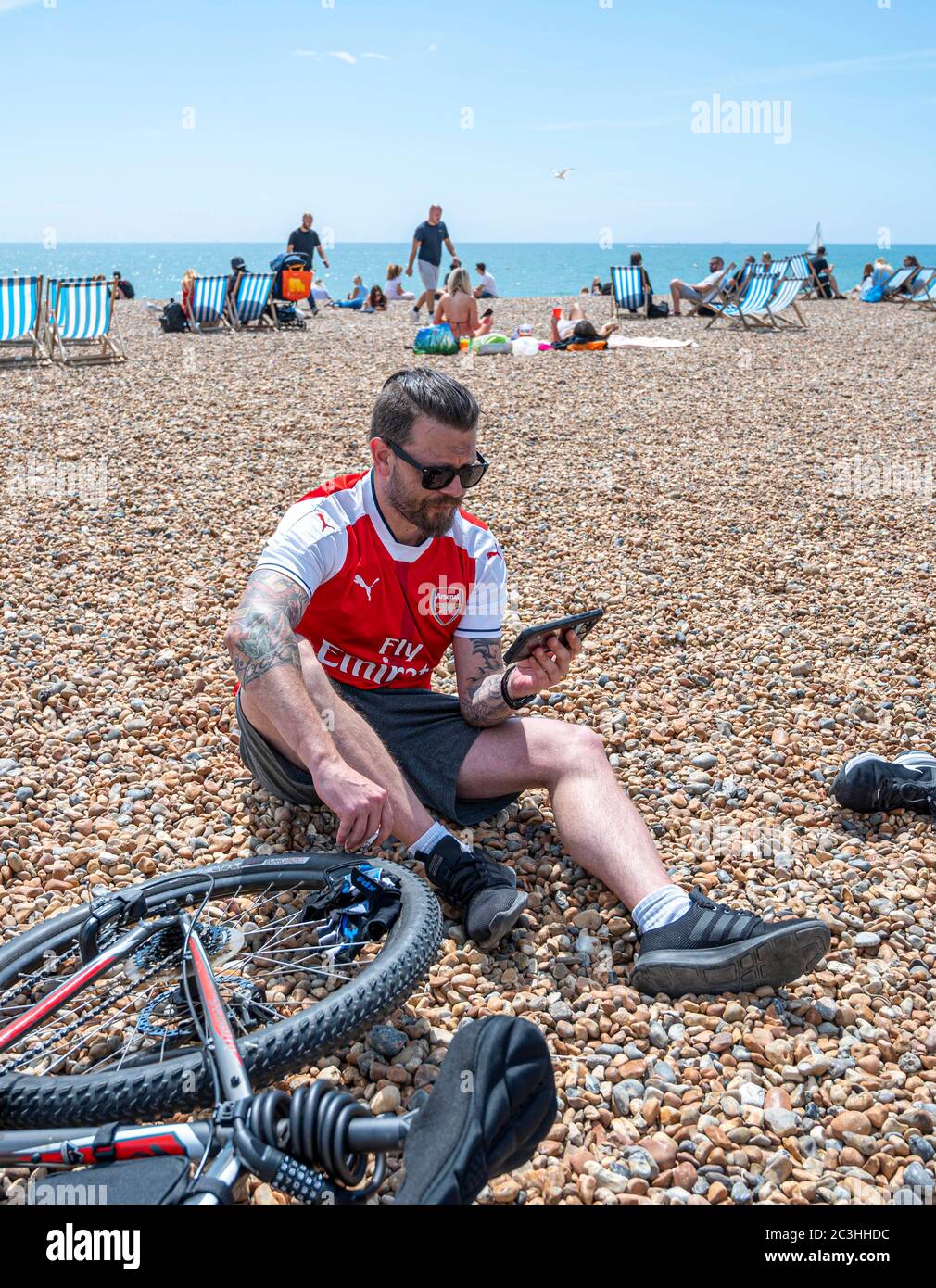 Brighton UK 20. Juni 2020 - ein Arsenal-Fußballfan spielt am Strand von Brighton mit seinem Handy und ist bereit, das Premier League-Spiel gegen Brighton heute während der Pandemiekrise des Coronavirus COVID-19 zu sehen. Alle Spiele werden hinter verschlossenen Türen wegen der Lockdown-Einschränkungen gespielt : Credit Simon Dack / Alamy Live News Stockfoto