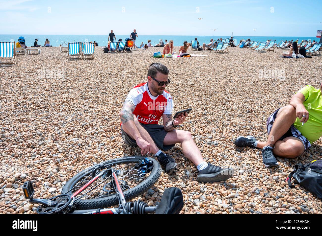 Brighton UK 20. Juni 2020 - ein Arsenal-Fußballfan spielt am Strand von Brighton mit seinem Handy und ist bereit, das Premier League-Spiel gegen Brighton heute während der Pandemiekrise des Coronavirus COVID-19 zu sehen. Alle Spiele werden hinter verschlossenen Türen wegen der Lockdown-Einschränkungen gespielt : Credit Simon Dack / Alamy Live News Stockfoto