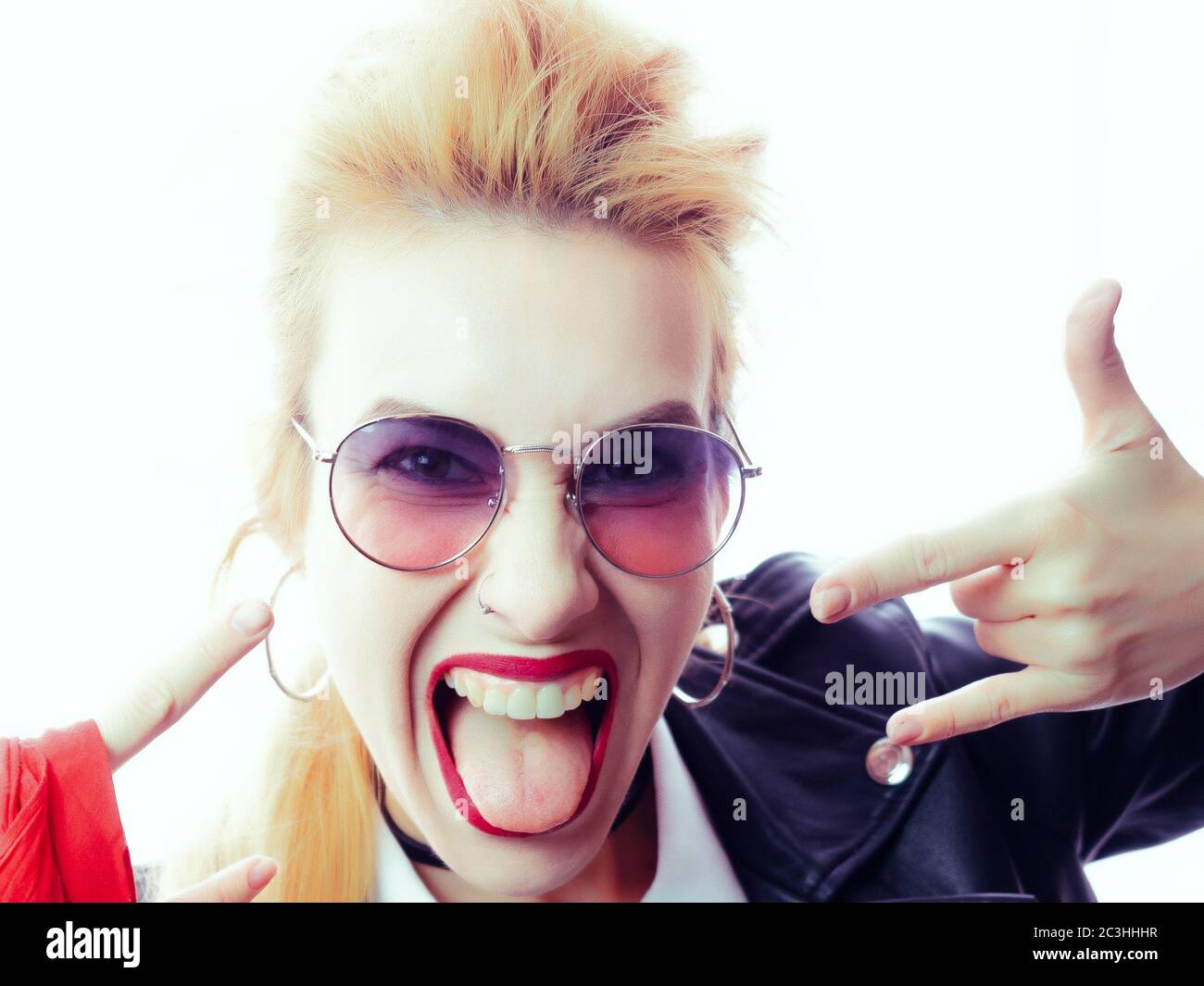 Schönes Mädchen in schwarzem Leder Jacke und Sonnenbrille zeigt Zunge und Hand Geste Rock Stockfoto