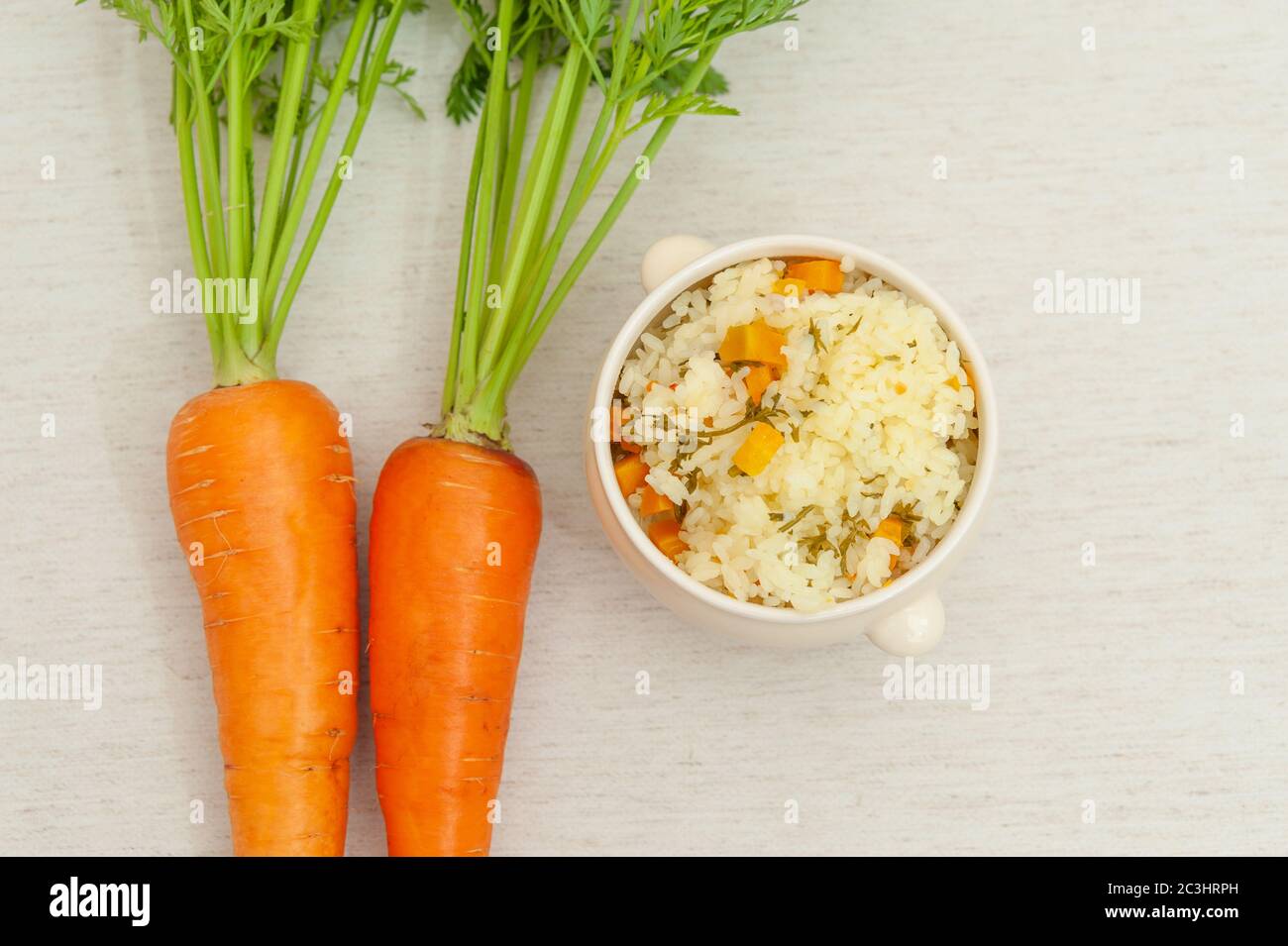 Vegetarische / vegane Küche - Rohe Karotten mit Blättern und eine Schüssel gekochten Reis mit Karotten. Isoliert auf weißem Hintergrund. Speicherplatz kopieren. Draufsicht. Stockfoto