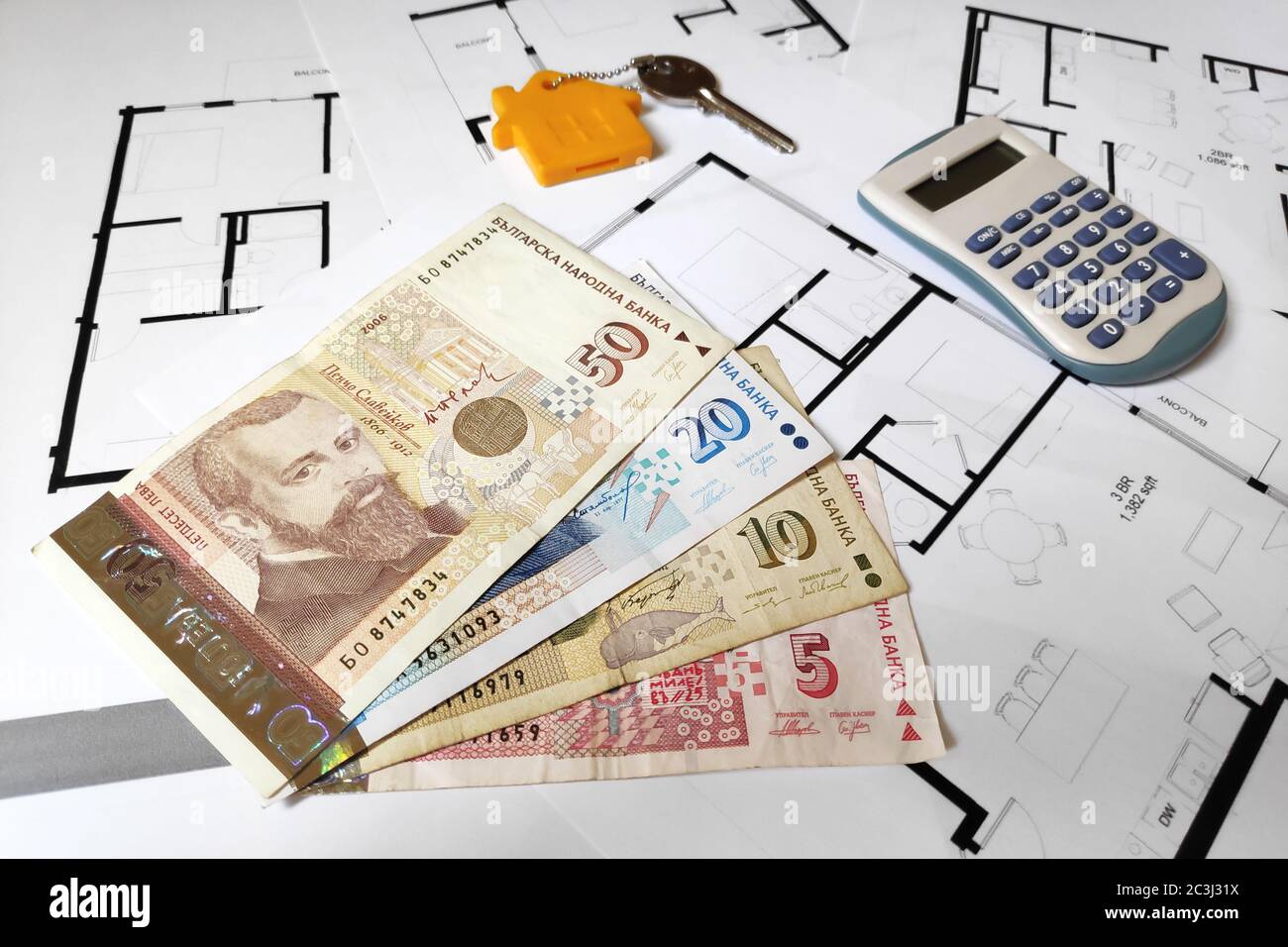 Nahaufnahme einiger bulgarischer Lew-Banknoten, eines Hausschlüssels und eines Rechners auf der Oberseite der Baupläne. Stockfoto