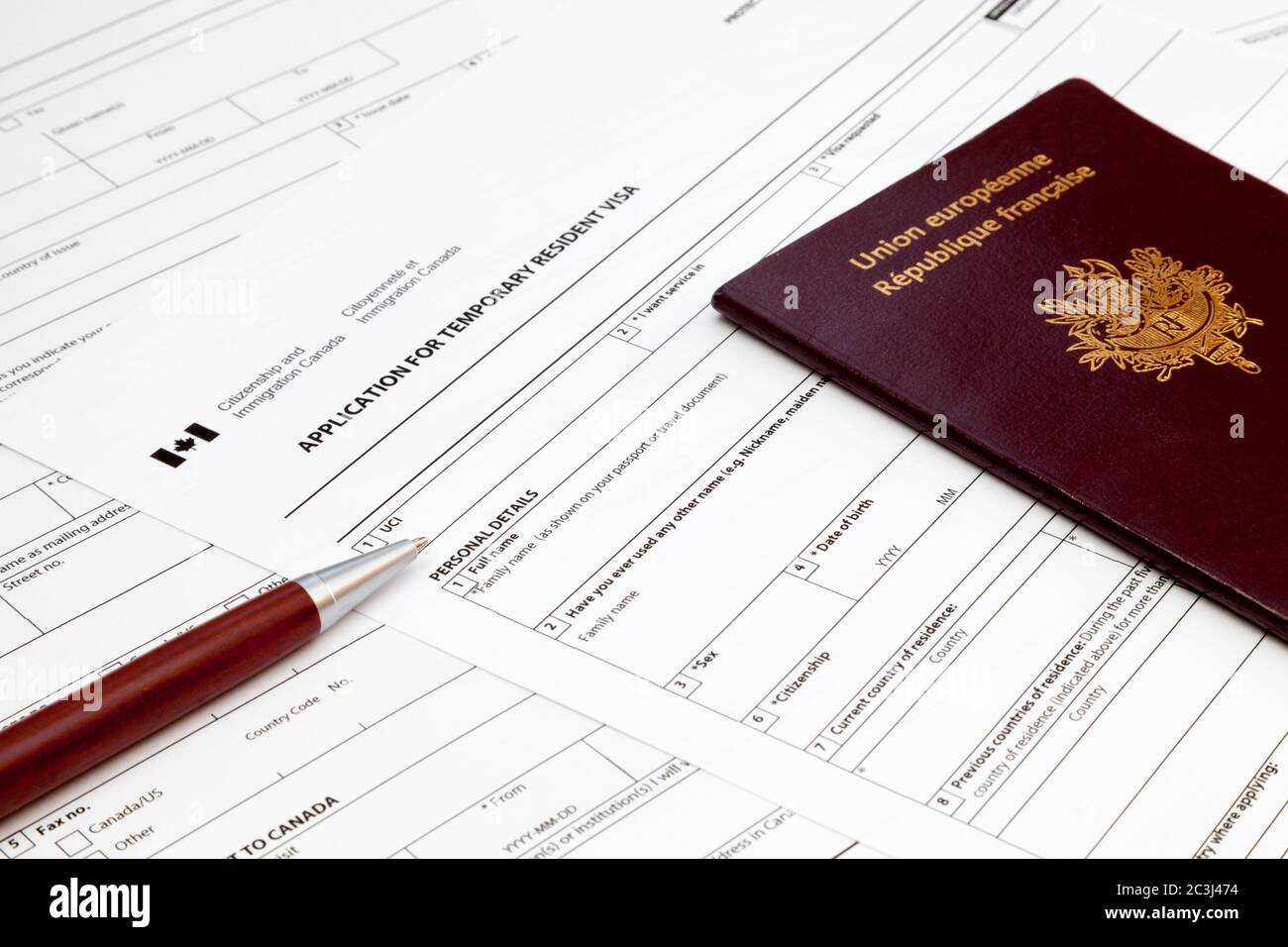 Ein Kugelschreiber und ein französischer Reisepass auf dem oberen Teil eines kanadischen Visum-Antragsformulars für vorübergehende Einwohner. Stockfoto