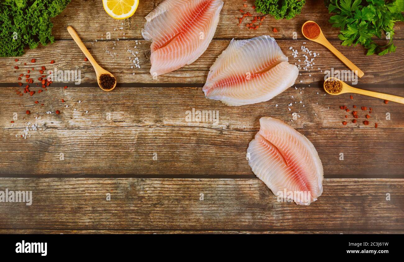 Rohe Tilapia Filets mit Gewürzen und Gemüse auf rustikalem Holztisch. Stockfoto