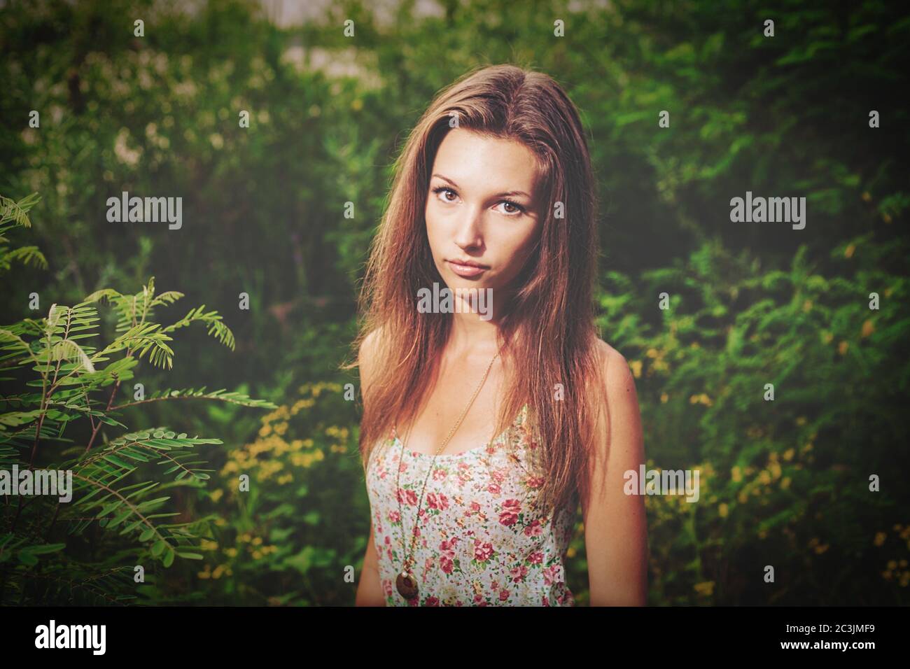 Blonde Mädchen in Boho Kleid und jevelry posiert in den Büschen im Sommer müde. Sie schaut ernsthaft auf die Kamera. Stockfoto